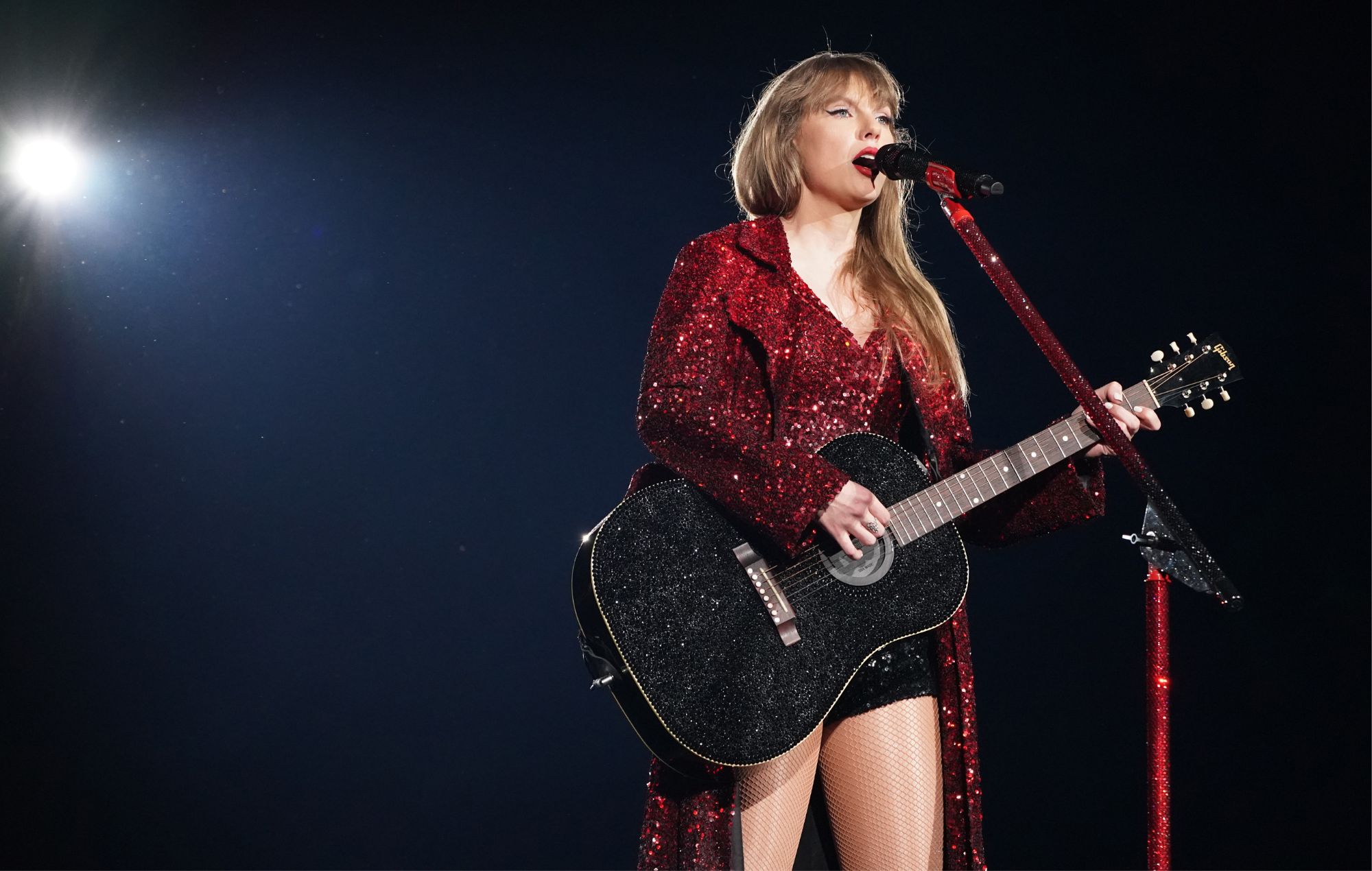 Taylor Swift performing in a showgirl-style outfit under orange lighting, hinting at her Super Bowl 2026 halftime show teasing